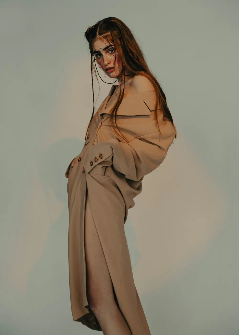 Model in a camel trench set against a soft green wall